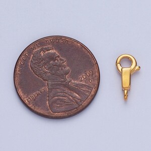 May include: Gold-toned metal clasp for jewellery making, shown next to a UK penny for size comparison.