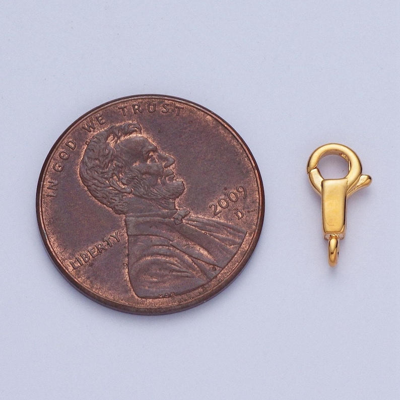 May include: Gold-toned metal clasp for jewellery making, shown next to a UK penny for size comparison.