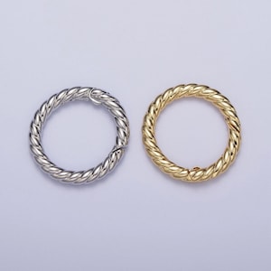 May include: Two round, textured metal clasps. One is silver-colored, and the other is gold-colored. The clasps have a twisted rope design and are likely used for jewelry or accessories.