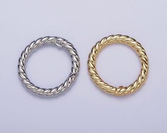 May include: Two round metal clasps with a twisted rope design. One is silver, the other gold. These clasps are likely used for jewellery or accessories. The clasps are approximately 3 cm in diameter.