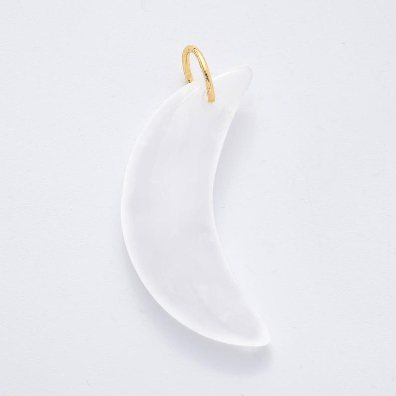 Op de afbeelding: Een maanvormige hanger van doorschijnend wit materiaal, met een goudkleurige lus aan de bovenkant. De hanger is glad en gebogen, tegen een witte achtergrond.
