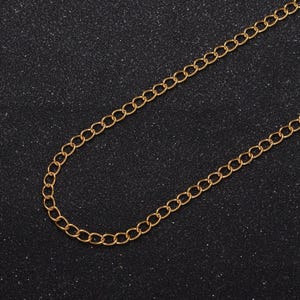 May include: A gold chain necklace with a classic curb link design. The chain is on a black background.