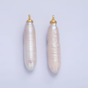May include: Two white baroque pearls with gold caps. The pearls are long and slender, with a slightly iridescent sheen.