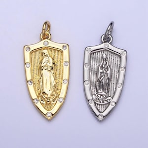 May include: Two silver and gold pendants in the shape of a shield with a religious figure inside. The pendants are adorned with small clear rhinestones around the edges.