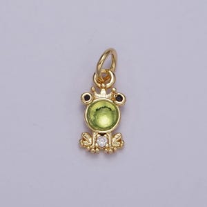 May include: A gold-tone frog charm with a green gem stone and a crown. The frog has black eyes and a white gem stone on its belly.