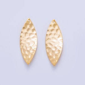 May include: Two gold-colored, leaf-shaped jewelry components. Each component has a hammered texture and a small hole at the top for attachment. The components are symmetrical and have a polished finish.