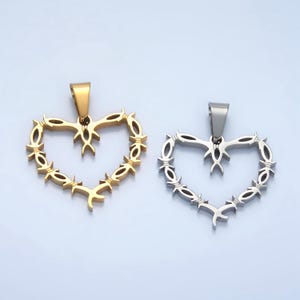 May include: Two heart-shaped pendants made of metal. One is gold and the other is silver. Both pendants are shaped like a heart with barbed wire around the edge.