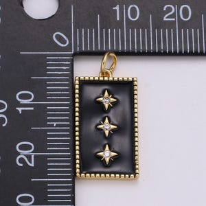 May include: Gold pendant charm with a black enamel rectangle featuring three gold stars with clear rhinestones. The pendant is approximately 1 inch in length.