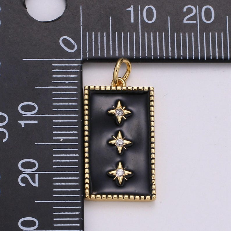 May include: Gold pendant charm with a black enamel rectangle featuring three gold stars with clear rhinestones. The pendant is approximately 1 inch in length.