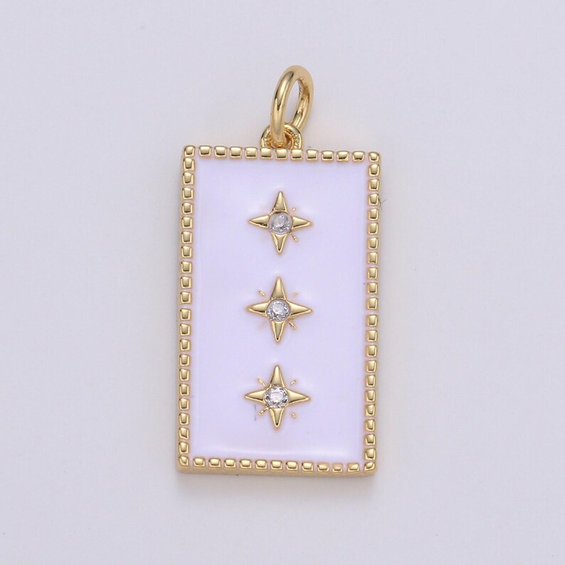 May include: Gold pendant charm with a white enamel rectangle featuring three gold stars with clear rhinestones. The charm has a gold loop for attaching to a necklace or bracelet.
