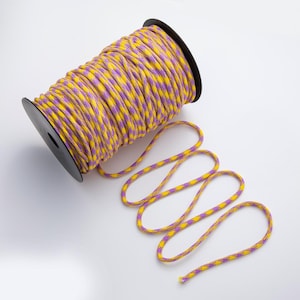 May include: A spool of yellow and purple patterned rope. The rope is wound around a black plastic spool. A length of the rope is unwound and lies on a white surface.
