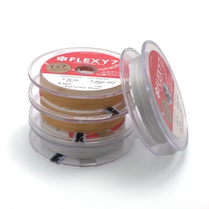 May include: Three spools of silver and gold colored nylon coated wire, labeled "FLEXY7" with the text "1x7 7strands" and "Coated Out Dia 0.35 mm (0.014 in) M. GOLD Stainless Steel" on the label. The spools are stacked on top of each other.