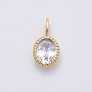 May include: A gold-toned pendant featuring a central oval-shaped clear faceted gemstone. The stone is encased in a metallic setting with a ribbed, textured border and includes a small vertical loop at the top for attachment to a chain or cord.