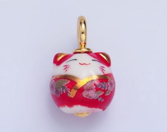 May include: A red and white ceramic charm in the shape of a cat wearing a red and gold kimono. The charm has a gold loop for hanging.