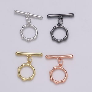 May include: Four toggle clasps in different finishes: silver, black, gold, and rose gold. Each clasp features a round, textured ring and a straight bar with a small ball at the end.