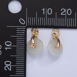 Pu&ograve; includere: Due ciondoli dorati con un disco bianco in giada e una pietra rosa. I ciondoli hanno un anello in cima per essere attaccati a una catena o un braccialetto.