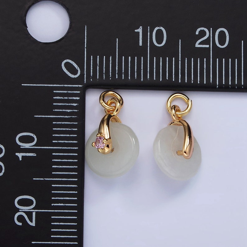 Pu&ograve; includere: Due ciondoli dorati con un disco bianco in giada e una pietra rosa. I ciondoli hanno un anello in cima per essere attaccati a una catena o un braccialetto.