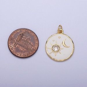 May include: Gold pendant charm with a white enamel background featuring a sun with a clear rhinestone center and a crescent moon. The pendant is approximately the size of a US penny.