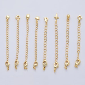May include: A collection of gold-colored chain extenders with various decorative charms. The charms include a heart, a teardrop, a tulip, a star, a heart, a cross, a ball, and a four-leaf clover. Each extender has a lobster clasp.