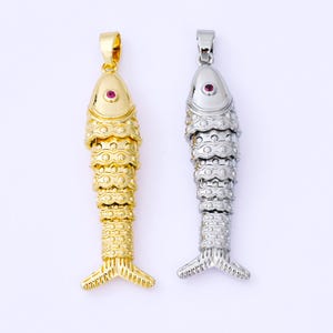 May include: Two fish-shaped pendants. One is gold-colored, the other is silver-colored. Both have a red gem eye and a detailed scale design. The pendants are likely for necklaces or bracelets.