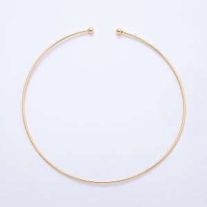 May include: A gold-colored choker necklace. The necklace is a simple, thin, circular design with a small ball at each open end. The jewelry is set against a white background.