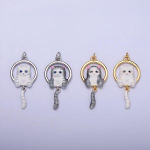 May include: Four silver and gold charm pendants featuring a white and gray cat with blue eyes and pink ears. The cat is hanging from a circle and has a tail that hangs down.