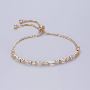 Puede incluir: Un brazalete ajustable de oro con una fila de piedras rectangulares transparentes.