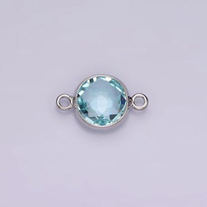 Puede incluir: Un conector plateado con una piedra redonda de color azul claro. El conector tiene dos bucles a cada lado para sujetarlo a joyas.