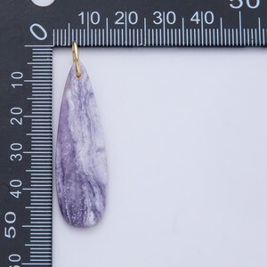 May include: A teardrop-shaped pendant with a gold-colored bail. The pendant is a marbled lavender color with white streaks. The pendant measures approximately 2 inches in length.