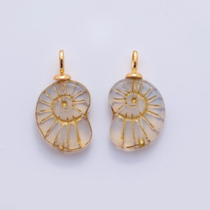 May include: Two gold-colored pendants with a spiral design. The pendants have a clear, light-colored center with gold-colored lines and a gold-colored loop at the top. The pendants are likely for jewelry.