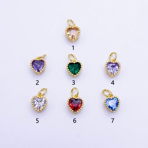 Pode incluir: Uma coleção de sete pingentes em forma de coração com engastes de metal dourado. Cada pingente apresenta uma pedra preciosa de cor diferente: pêssego, roxo, verde, roxo claro, branco, vermelho e azul. Os pingentes são numerados de 1 a 7.