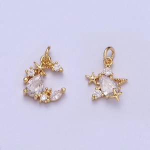 May include: Two gold-tone charms featuring a crescent moon and a star with clear crystal accents. Both charms have a loop for attaching to a bracelet or necklace.