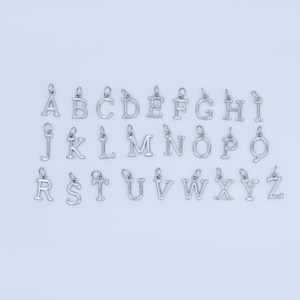 Könnte beinhalten: Eine Sammlung silberfarbener Buchstabenanhänger, jeweils mit einer kleinen Schlaufe zum Befestigen an einer Kette oder einem Armband. Die Buchstaben A bis Z sind abgebildet, ideal für personalisierten Schmuck.