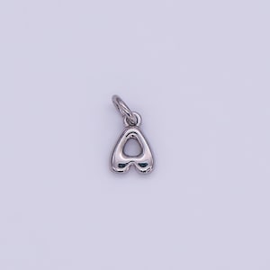 May include: A silver-colored charm in the shape of the letter "A". The charm has a rounded, bubble-like design with a small loop at the top for attaching to a chain or bracelet. The background is a solid, light purple color.