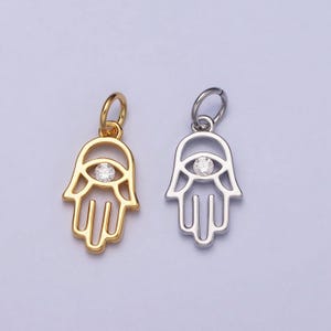 May include: Two hamsa hand charms with a clear crystal eye in the center. One charm is gold and the other is silver.
