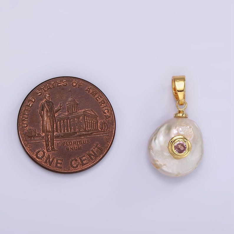 May include: A gold pendant with a baroque pearl and a pink gemstone set in a gold bezel. The pendant is hanging from a gold chain.