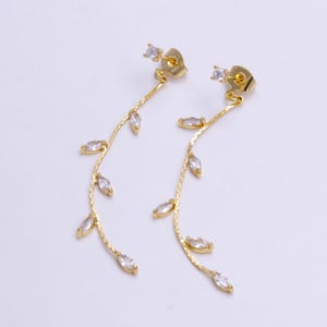 May include: A pair of gold dangle earrings with a delicate chain and marquise-shaped clear crystals. The earrings have a leaf-like design.