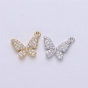 May include: Two butterfly charms, one gold and one silver, with clear crystal accents. Both charms have a loop for attaching to jewelry.