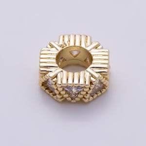 May include: A gold-toned metal bead with a cylindrical shape, featuring a series of vertical bars and small spheres along the outer edge. The center of the bead is hollow, and clear, triangular-cut stones are set between the metal segments.