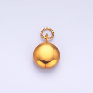 May include: A gold-colored pendant with a circular charm and a small loop at the top. The charm is a smooth, reflective sphere. The pendant hangs against a light background.