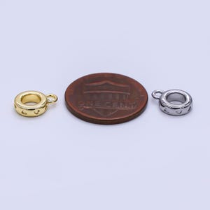 May include: Two small, round metal charms with a loop for attaching to jewelry. One charm is gold-colored, the other is silver-colored. Both have a series of small cut-out designs around the edge. A penny is next to the charms for size comparison.