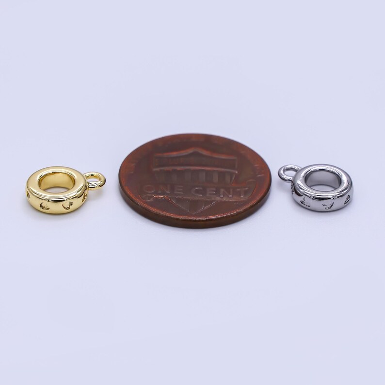 May include: Two small, round metal charms with a loop for attaching to jewelry. One charm is gold-colored, the other is silver-colored. Both have a series of small cut-out designs around the edge. A penny is next to the charms for size comparison.
