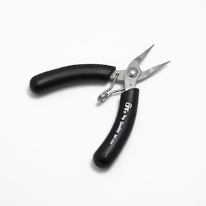 May include: Needle-nose pliers with black handles and silver metal jaws. The pliers are open, displaying the pointed tips. The text "Gr Top Quality MP-104" is printed on one handle. The tool is designed for precision work.