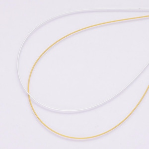 Puede incluir: Primer plano de dos alambres finos y curvados. Uno es de color dorado brillante y el otro es plateado. Los alambres están sobre un fondo blanco liso. La imagen está bien iluminada y los alambres están enfocados.