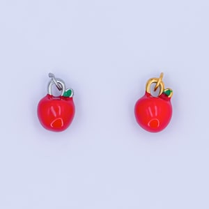 May include: Two red apple charms with green leaves. One charm has a silver loop and the other has a gold loop.