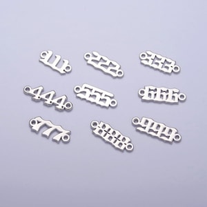 May include: Silver-toned metal number charms with a gothic font style. The charms feature the numbers 111, 222, 333, 444, 555, 666, 777, 888, and 999.