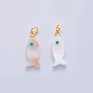 May include: Two fish-shaped pendants. Each pendant is made of iridescent white material with a gold-coloured loop at the top. A small green dot is centered on each fish. The fish have a small tail fin.