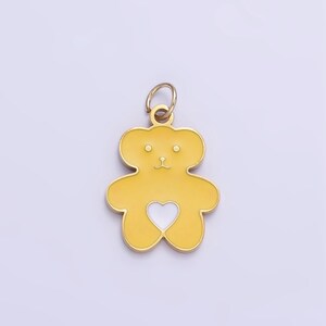 Op de afbeelding: Een gouden hanger in de vorm van een teddybeer met een wit hart op zijn borst. De hanger heeft een lus aan de bovenkant om aan een ketting of armband te bevestigen.