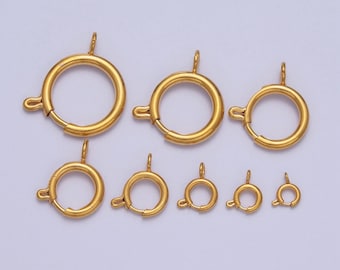 Pode incluir: Conjunto de oito fechos de metal dourado de tamanhos diferentes. Os fechos são redondos com um pequeno laço na parte superior para prender a uma corrente ou cordão.