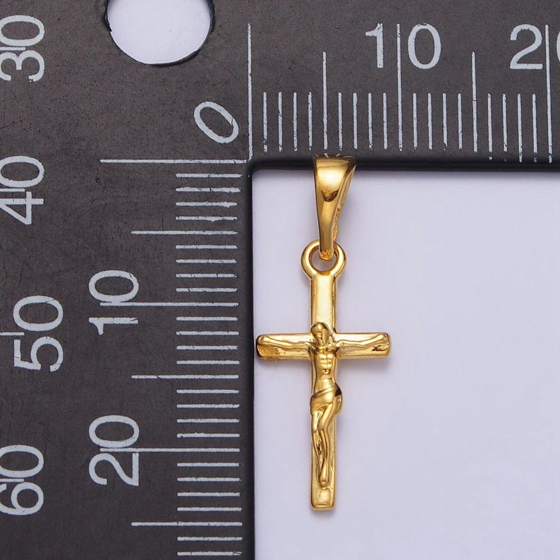 May include: A gold-colored crucifix pendant featuring a detailed depiction of Jesus on the cross. The pendant is suspended from a small loop and is shown against a white background. The pendant's dimensions are not visible.